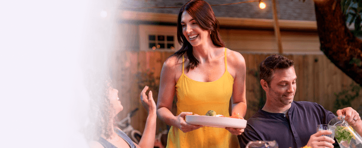 A woman carrying a plate while talking and laughing with people dining together outside.