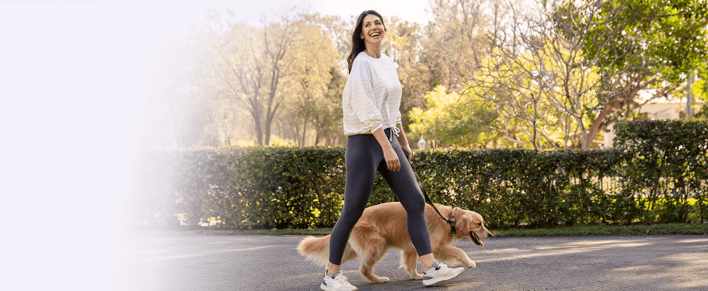 A woman walking her golden retriever in a park