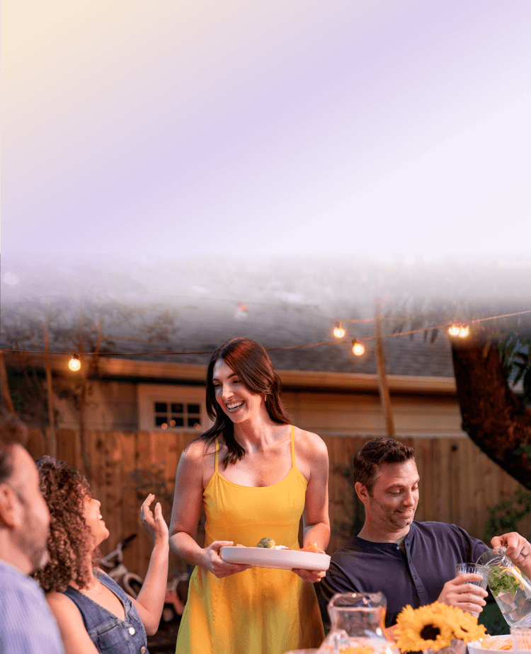 A woman carrying a plate while talking and laughing with people dining together outside.