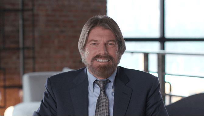 Man in blue suit with a black, patterned tie who is smiling