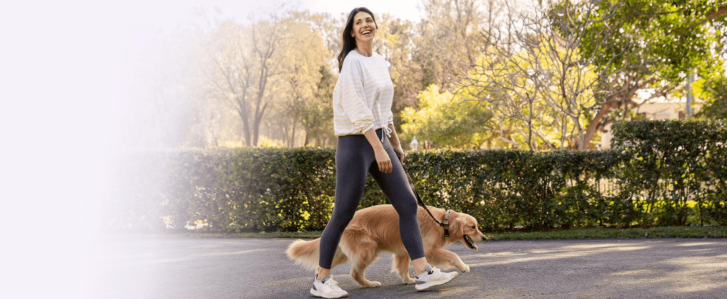 A woman walking her dog in a park on a sunny day